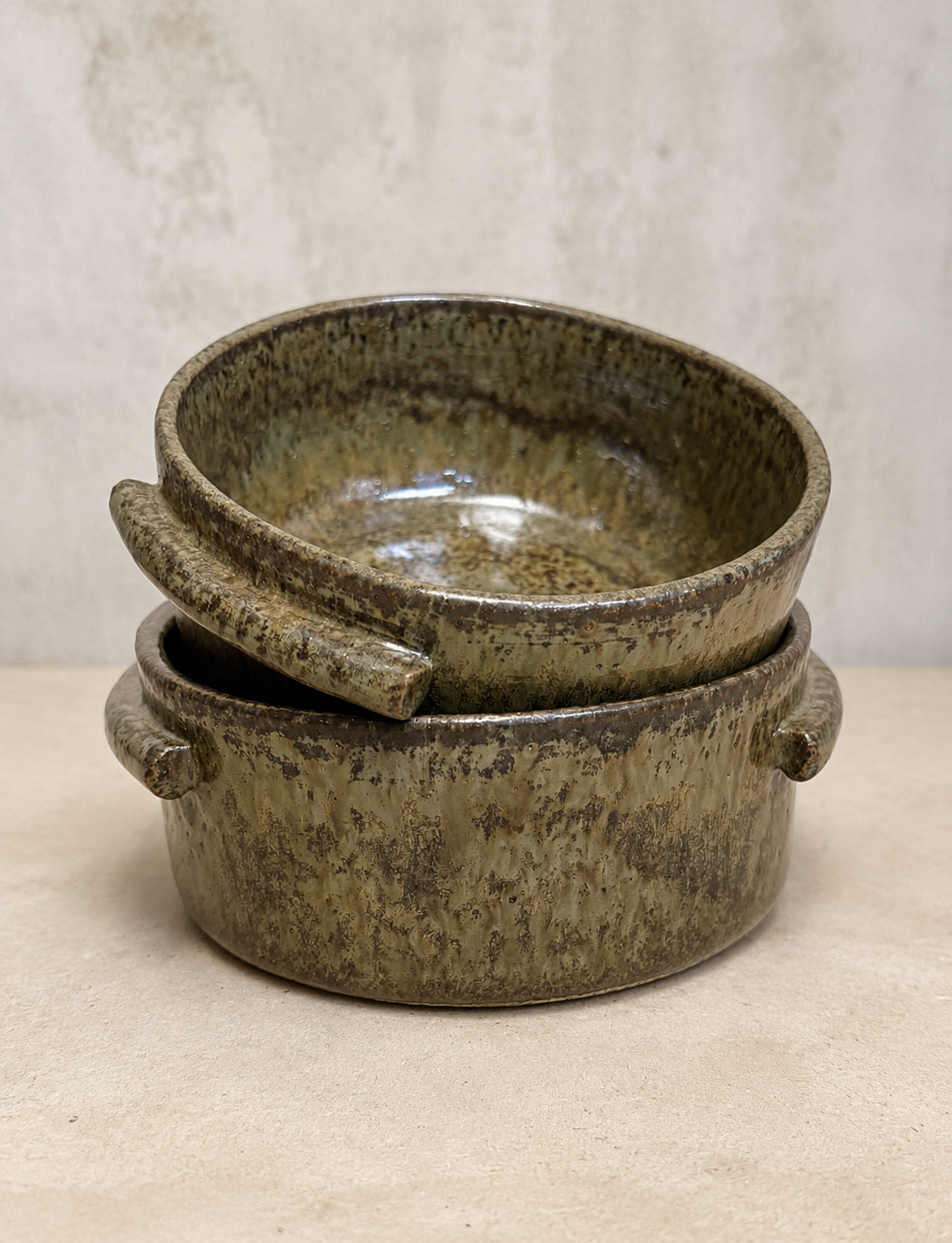 Two stacked speckled olive stoneware bowls with side handles