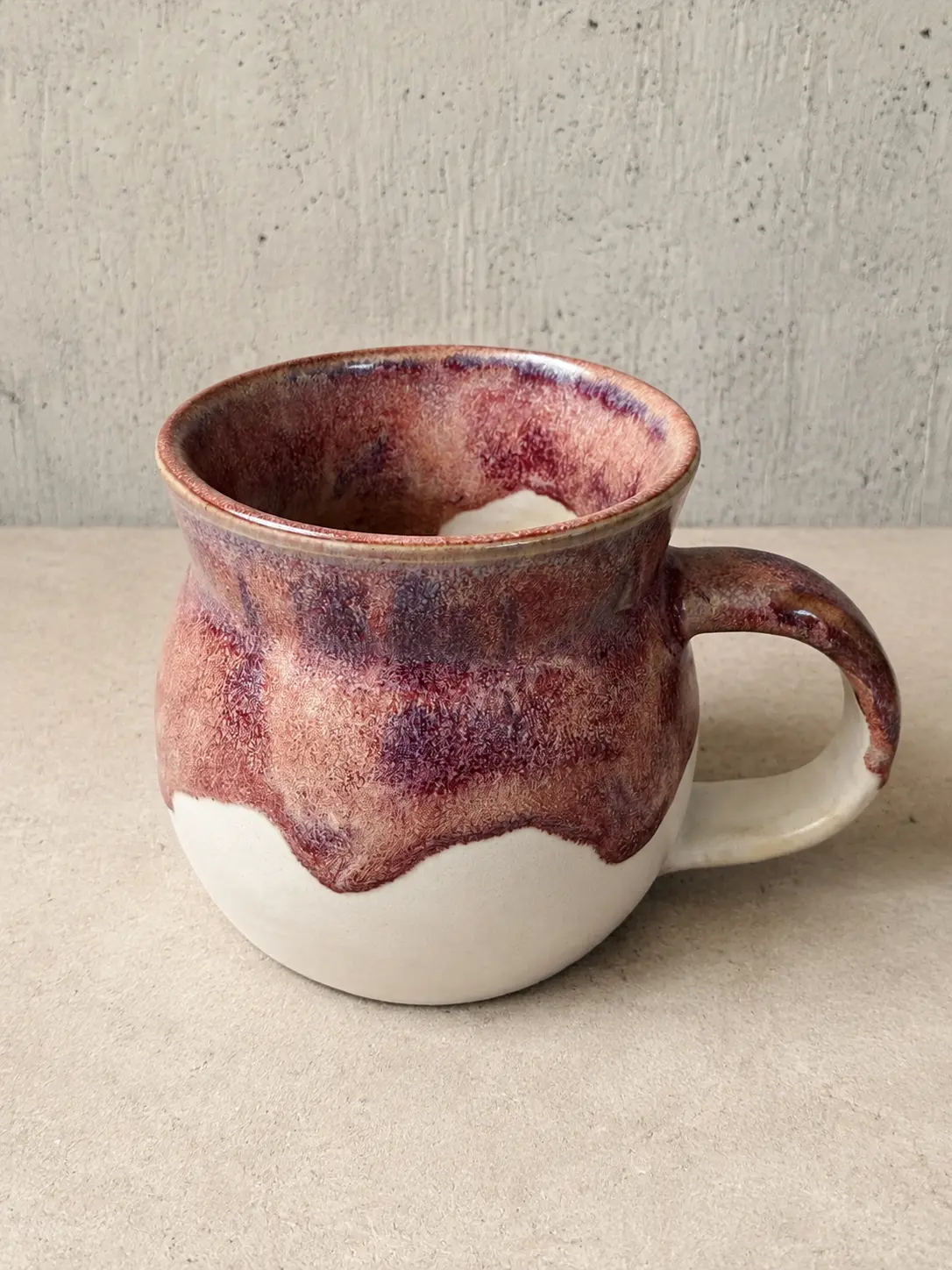 Rounded mug with plum and rust glaze dripping over raw stoneware