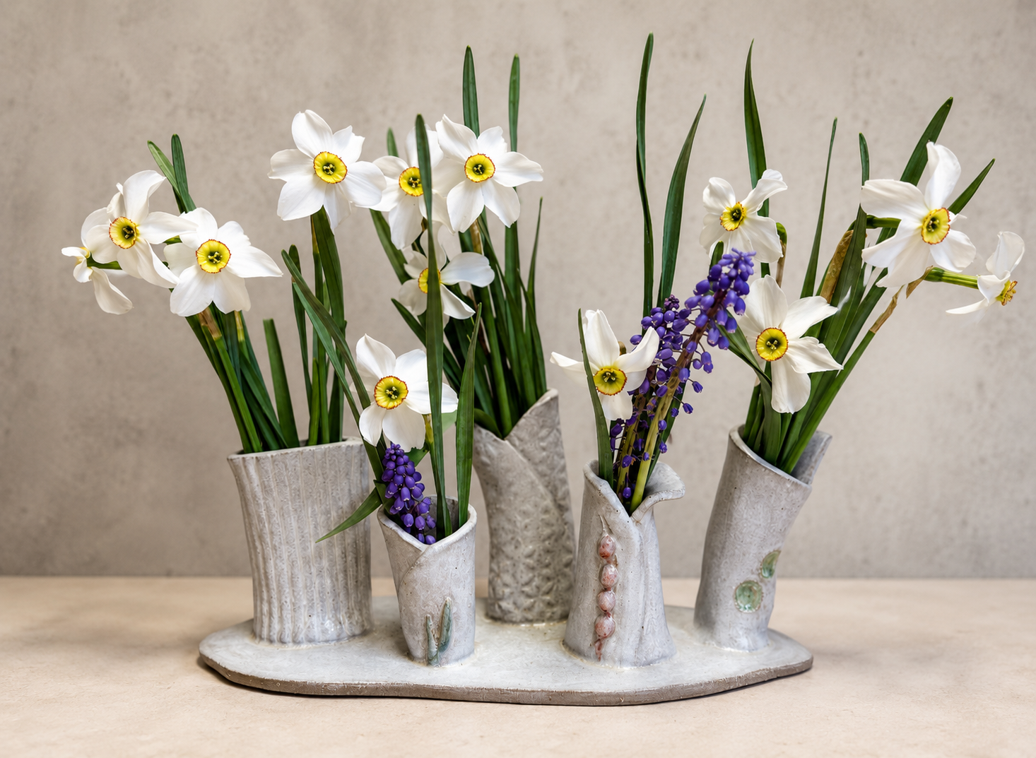 Cluster of small textured bud vases on a ceramic base holding daffodils